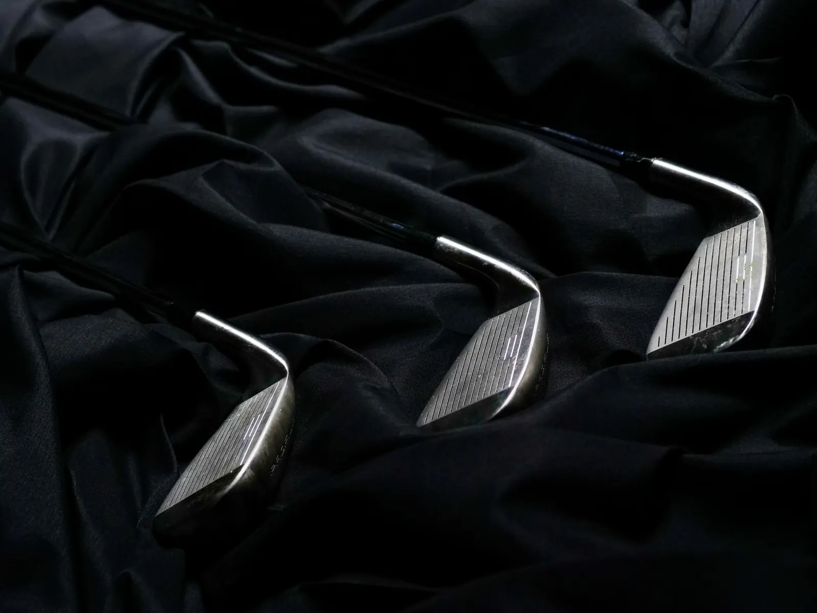 Three golf irons laid on a dark cloth